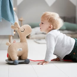 Toddler playing with Done By Deer Pull Along 2-in-1 soft toy, encouraging first steps with a cute giraffe design.