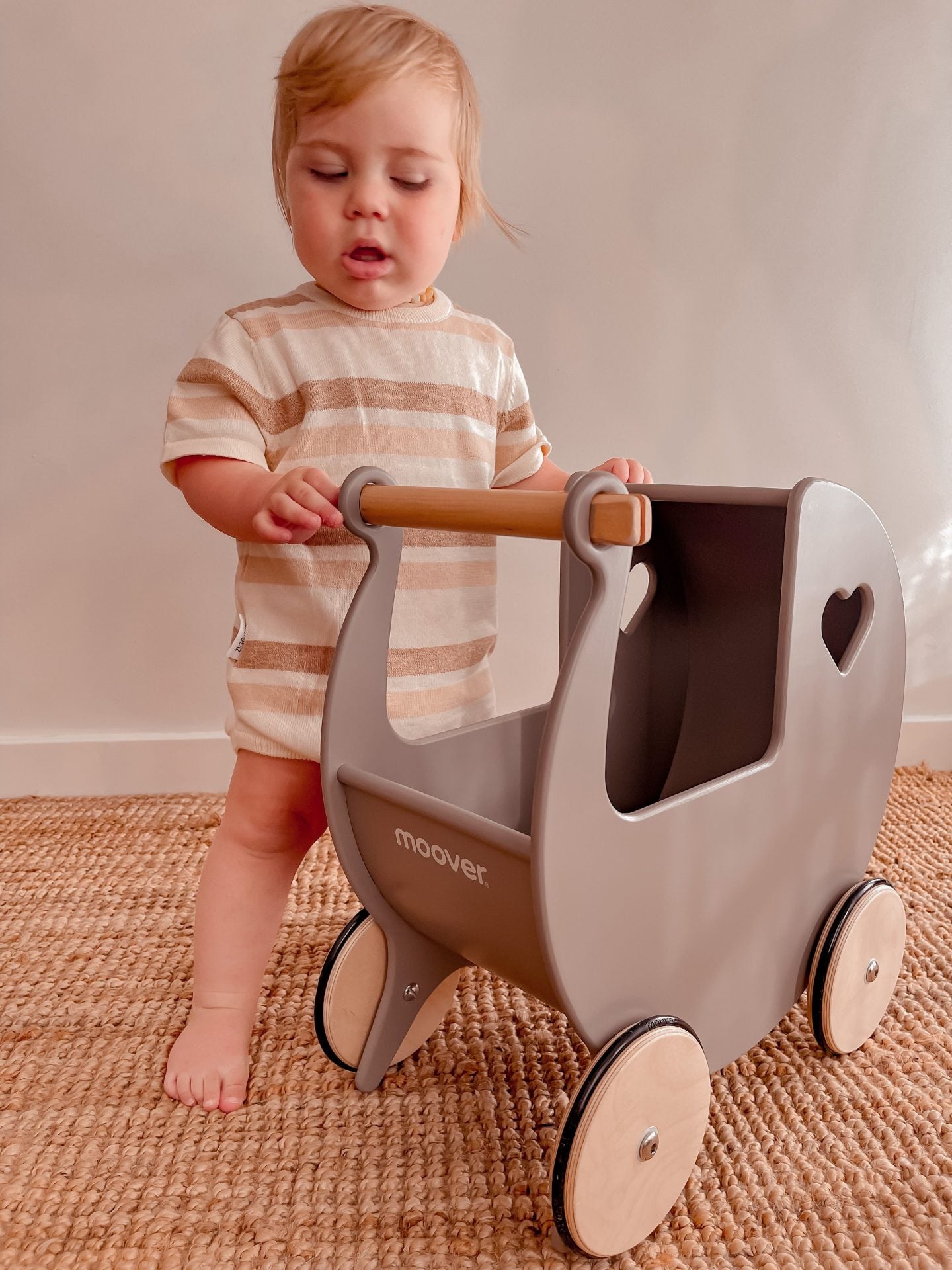 Toddler playing with a classic Moover toy pram, showcasing its sturdy design and wooden handle.