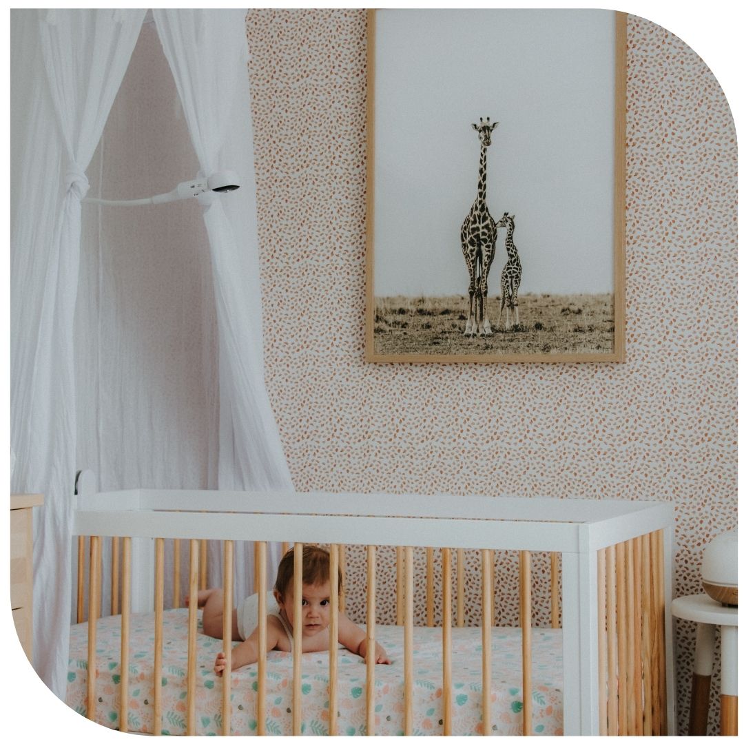 Baby in crib with giraffe artwork in nursery, featuring Oricom 5" Smart HD Baby Monitor for safety and clarity.